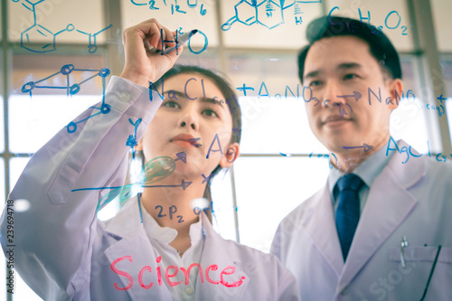 A handsome asian professor proud to teaching biology and chemist for young beautiful girl scientist to writing table of the elements on glass board in laboratory at morning classroom.