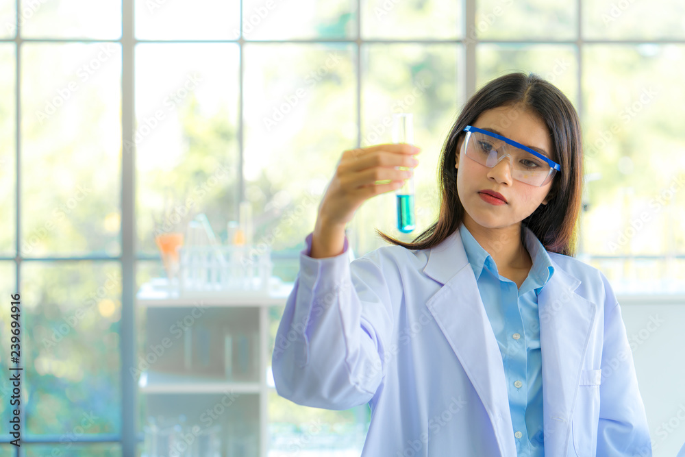 A young beautiful asian woman scientist watching result glass tube with blue liquid substance in chemistry experiment in hospital lab. Portrait of science & healthcare concept. Soft and clean filter.