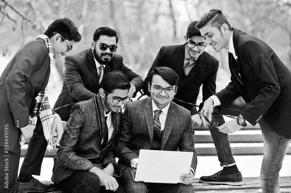 Fototapeta premium Group of six indian businessman in suits posed outdoor in winter day at Europe, looking on laptop.