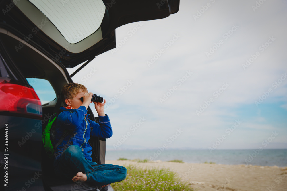 young boy looking through binoculars travel by car at sea