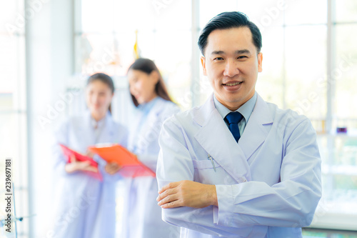  A middle aged man scientist smiling happily with his arms crossed posing at her laboratory colleagues. A confident professor CEO standing preparing equipment for teaching collage student. Copy space.