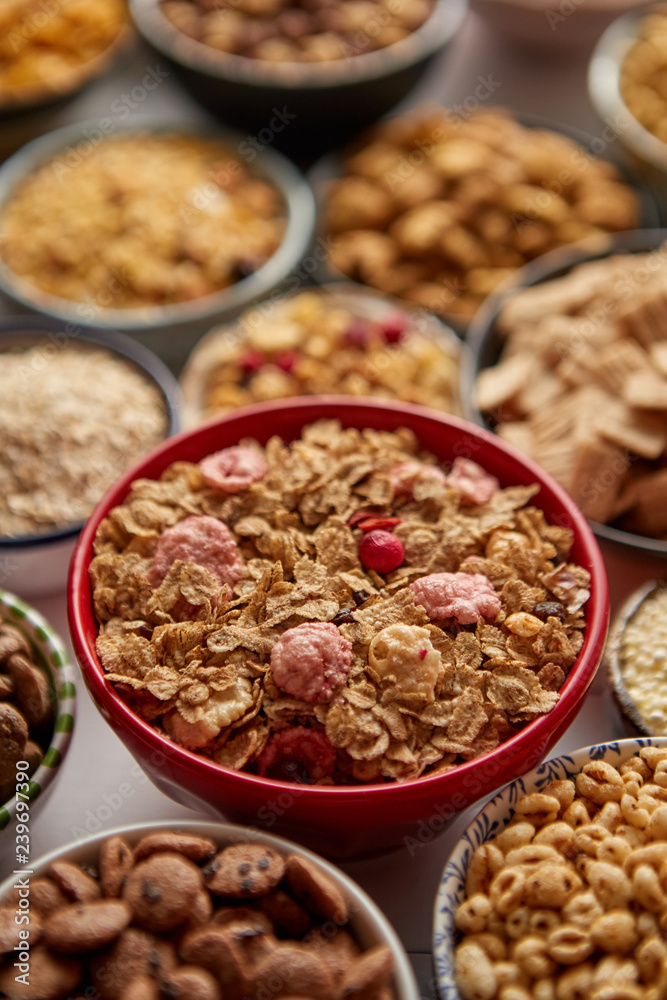 Close up and selective focus. Composition of different kinds cereals placed in ceramic bowls with cornflakes, granola, cereals and oatmeal. Flat lay, top view on white wooden table. Close up and selective focus. Composition of different kinds cereals placed in ceramic bowls with cornflakes, granola, cereals and oatmeal. Flat lay, top view on white wooden table.