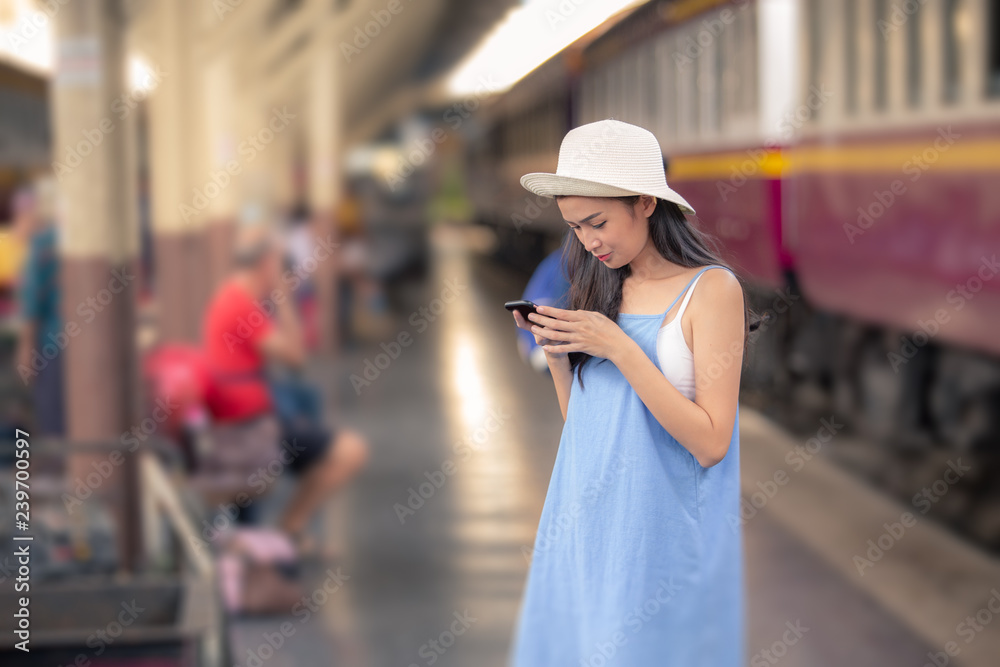 A beautiful charming asian girl with white panama hat and light blue dress standing beside train station platform. Using smart mobile phone. Feeling look happy and relax. Portrait lady travel concept. A beautiful charming asian girl with white panama hat and light blue dress standing beside train station platform. Using smart mobile phone. Feeling look happy and relax. Portrait lady travel concept.