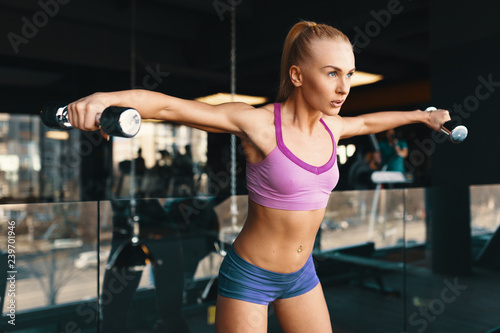 Young Caucasian woman doing exercise with dumbbells while traini