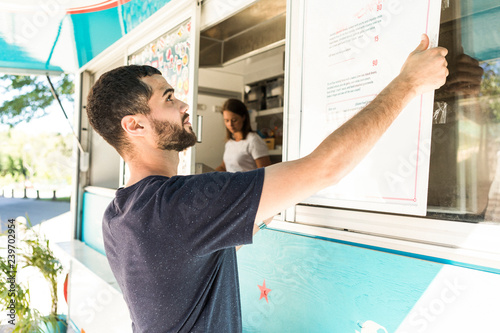 Confident young male salesman positioning menu placard on food truck