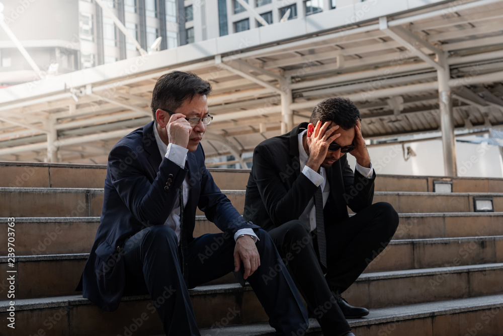 Asian business man sitting on a staircase between a tall building, stressed and fear by a business problem, Unsuccessful and unemployed, to strain concept.