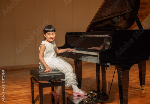 Little girl in white dress on stage with grand piano