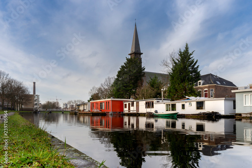 Reflection of the Leiden Church in canal water with white and red houseboats