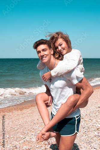 A guy carrying a girl on his back, at the beach, outdoors