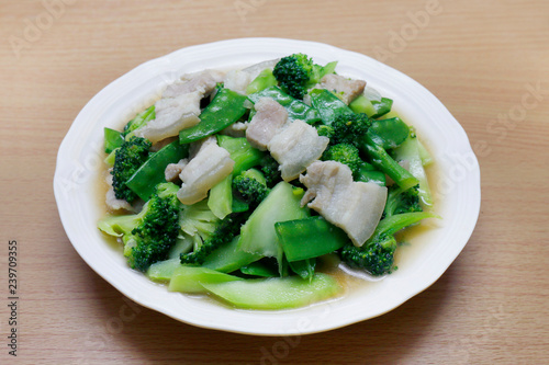 Stir Fried Broccoli, Peas with Crispy Pork with oyster sauce, Fried vegetable broccoli for food menu diet healthy in a dish on a wooden floor (Thai Foods)