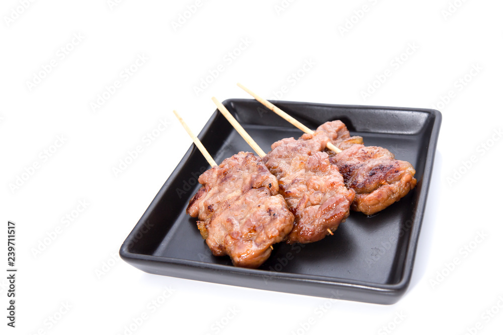 Pork barbecue sticks served on black square plate on isolated white background.