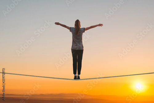 A girl stands on the rope and raises her hands against the sunset. The concept of freedom and confidence. photo