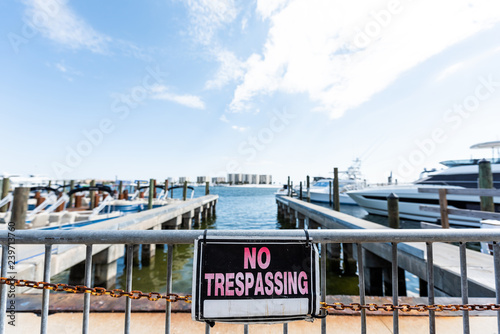 Destin, USA closeup of city town village harbor with sign for No Trespassing during sunny day in Florida panhandle gulf of mexico, metal fence