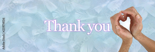 Thank you from my heart - female hands making a heart shape against a pale blue randomly scattered feather background with the words THANK YOU and copy space
