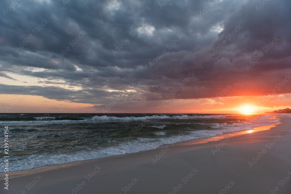Dramatic dark orange red sunset in Santa Rosa Beach, Florida with Pensacola coastline coast cityscape skyline in panhandle with ocean gulf of mexico hurricane