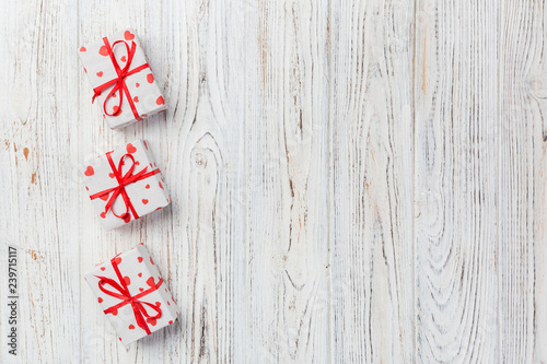 Valentine or other holiday handmade present in paper with red hearts and gifts box in holiday wrapper. Present box of gift on white wooden table top view with copy space, empty space for design