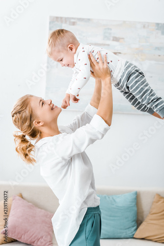 attractive woman raising toddler son and smiling in living room