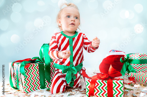 Cute baby girl 1 year old near santa hat posing over Christmas decoratins. Sitting on floor with Christmas ball. Holiday season. photo