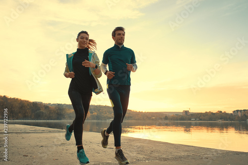 Young man and woman out for a run on the lake at the sunrise