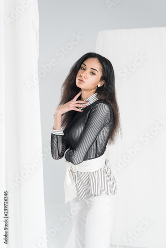 sensual beautiful african american girl in stylish clothes standing near tulle on white