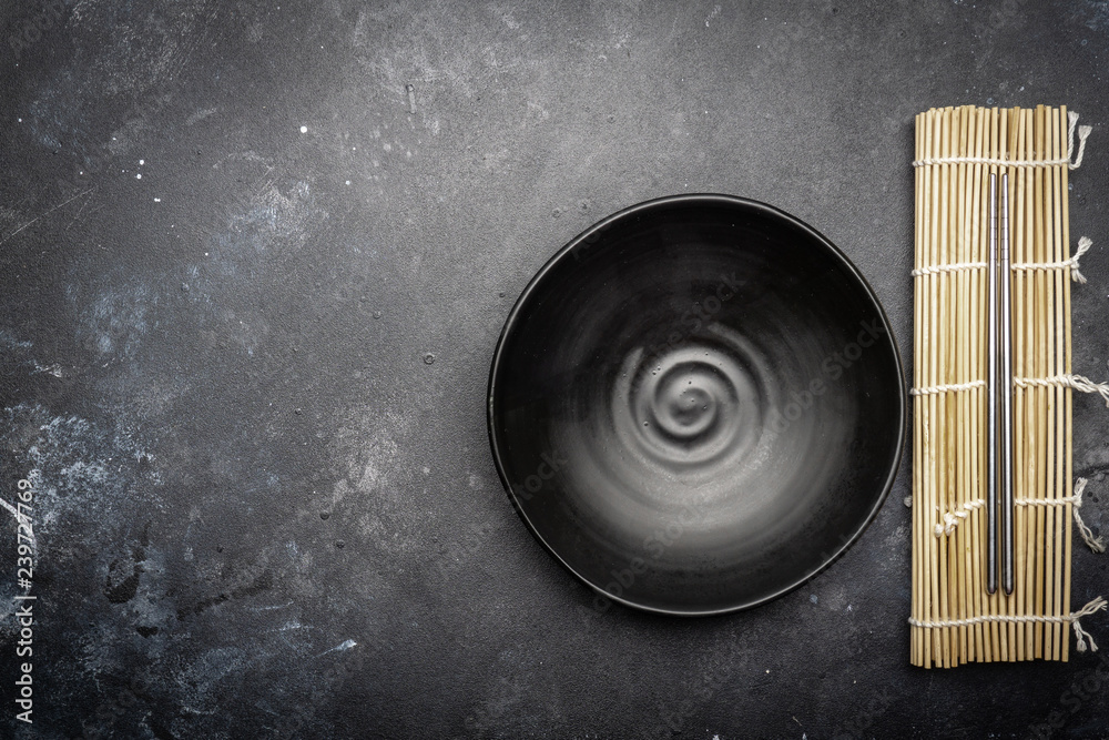 Obraz premium Empty plate (dark) and Chinese chopsticks on a dark background. Asian style, Asian cuisine. Copy space.