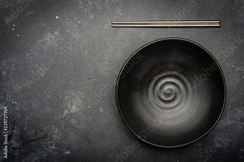 Empty plate (dark) and Chinese chopsticks on a dark background. Asian style, Asian cuisine. Copy space.