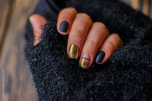 Luxury short manicure on a dark wooden background. Black matt nails design with golden color. 