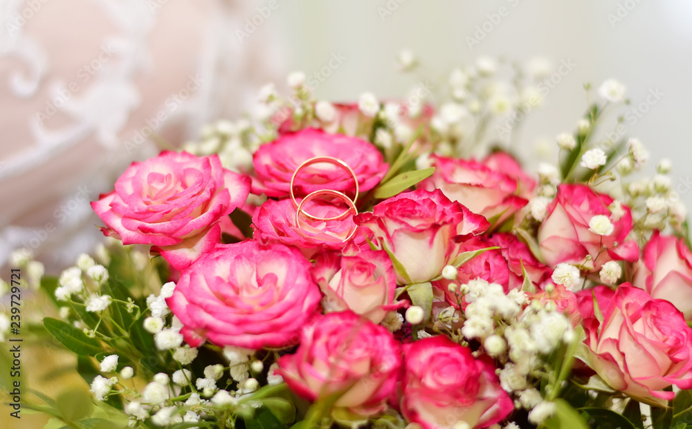 A bouquet of pink roses, wedding rings are on the bouquet.