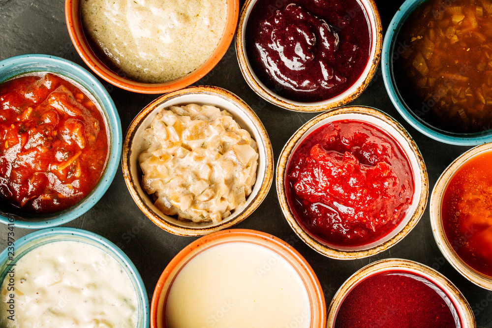 Set of different sauces on black wooden background.