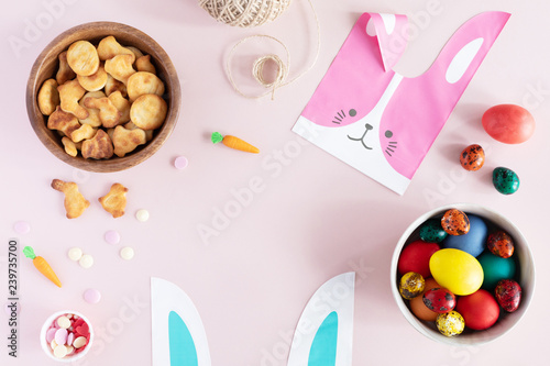 Flat lay of arrangement decorations for Happy Easter holiday. Springtime background. Top view of colorful eggs, bunny bag, cookies on pastel pink table desk.