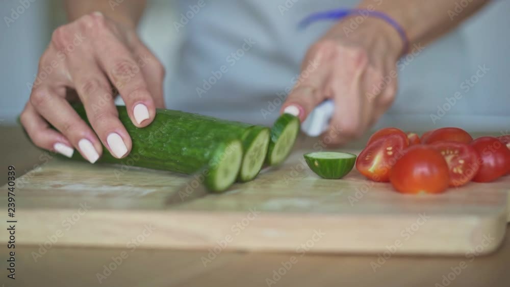 Hands of unrecognizable woman wearing gray apron cutting cucumber on cutting board. Slider real time close up shot