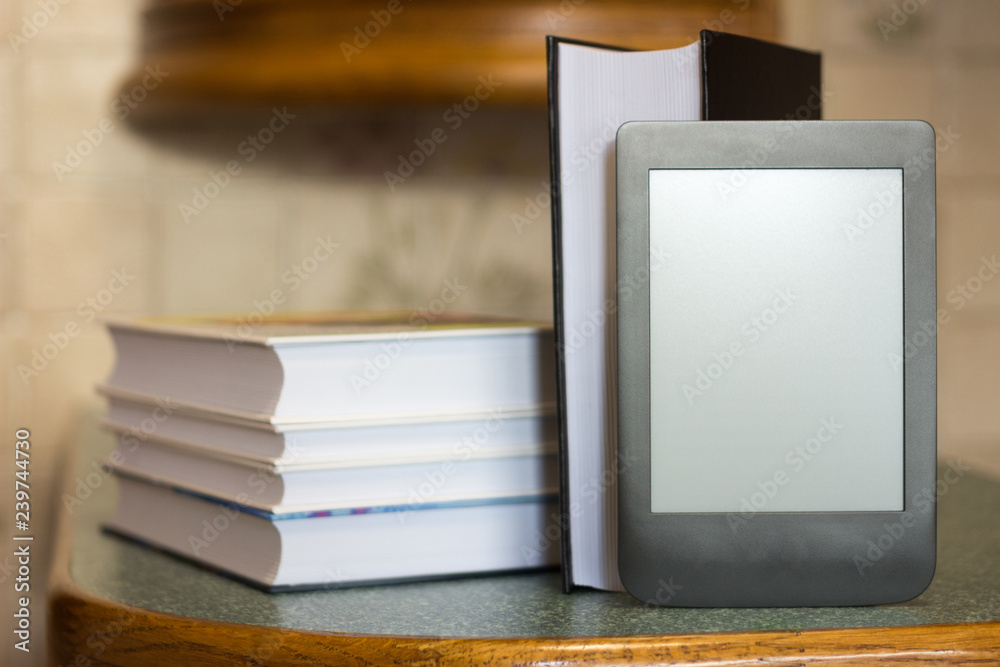 Modern e-book on the background of a stack of thick paper books. Close-up with selective focus. Training and technology concept Modern e-book on the background of a stack of thick paper books. Close-up with selective focus. Training and technology concept