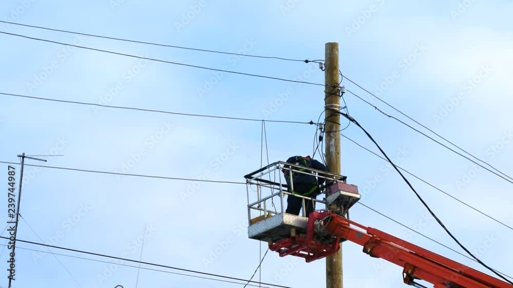Electricians in uniform repair power lines, standing on the bucket. Winter day. Cold weather. In the background is a blue cloudy sky. Electricians in uniform repair power lines, standing on the bucket. Winter day. Cold weather. In the background is a blue cloudy sky.