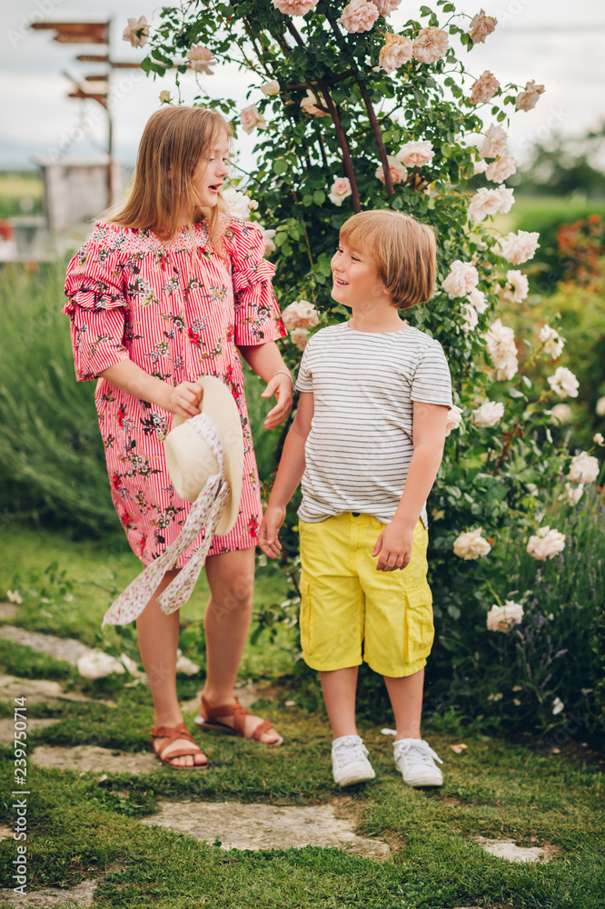 Fototapeta premium Summer portrait of two stylish kids posing in flower garden on a nice sunny day