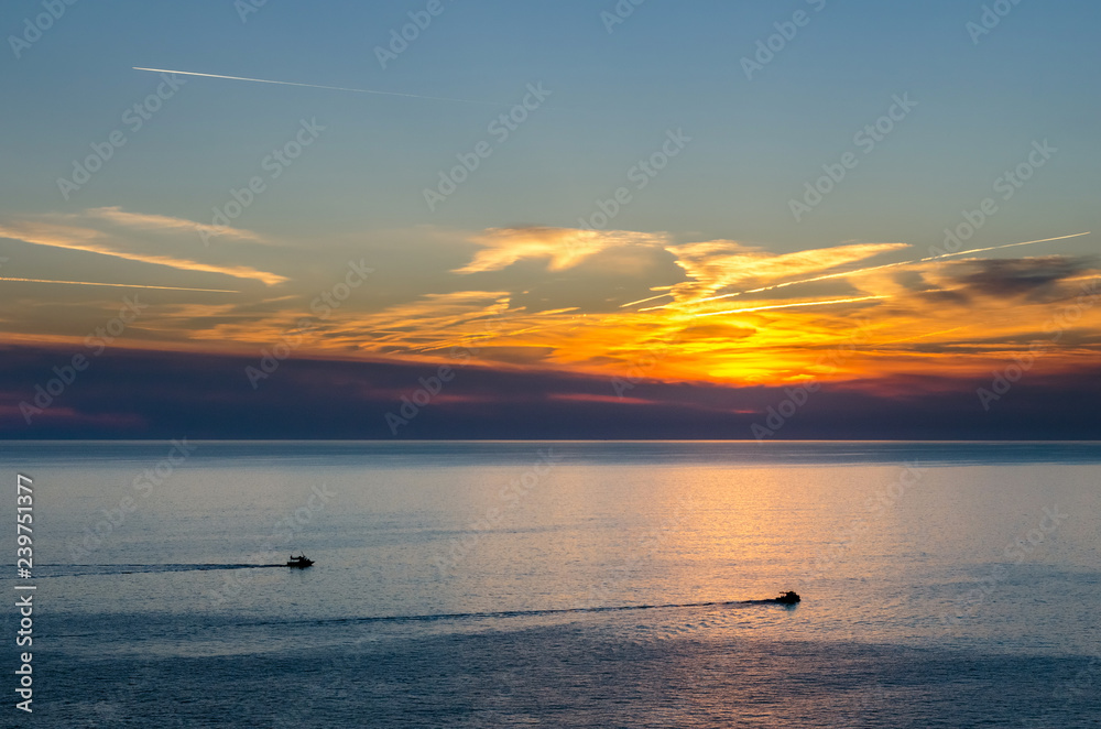 Sunset under the sea with moving pleasure boats and vapour trails on twilight sky Sunset under the sea with moving pleasure boats and vapour trails on twilight sky
