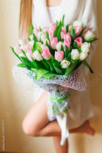 Woman holding a large bouquet of pink and white tulips and green on a background of beautiful legs. Spring bride bouquet. Happy women's day.