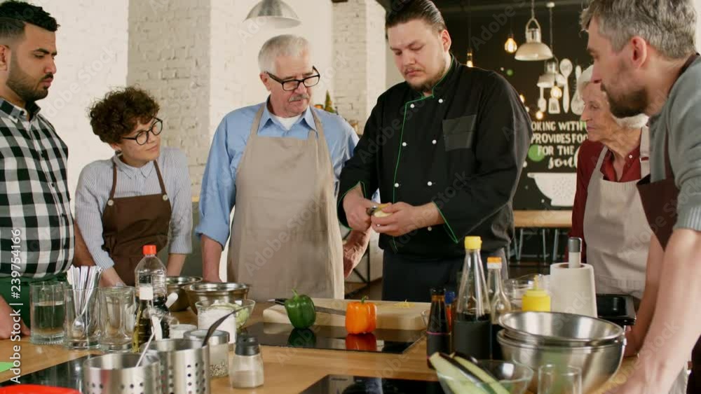 Medium shot of people of different ages and nations gathered around male chef who is showing how to peel lemon Medium shot of people of different ages and nations gathered around male chef who is showing how to peel lemon