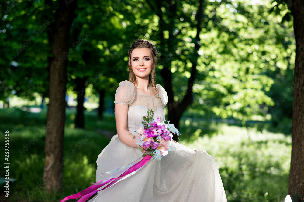 Stylish and beautiful bride walks in a flowered park with a wedding bouquet. Bride with long flowing hair. The most important day in the life of a girl. Stylish and beautiful bride walks in a flowered park with a wedding bouquet. Bride with long flowing hair. The most important day in the life of a girl.