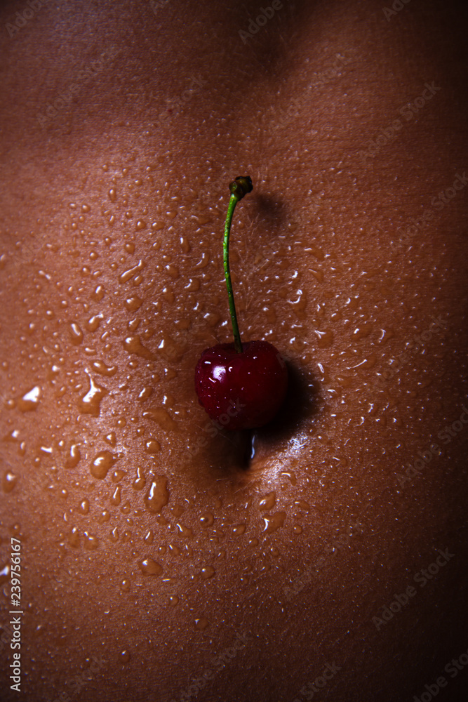 Foto de The belly of a dark-skinned woman with cherries and drops of water. Sexy  girl closeup. African American pretty girl. Cherry for dessert. Erotic  concept. do Stock