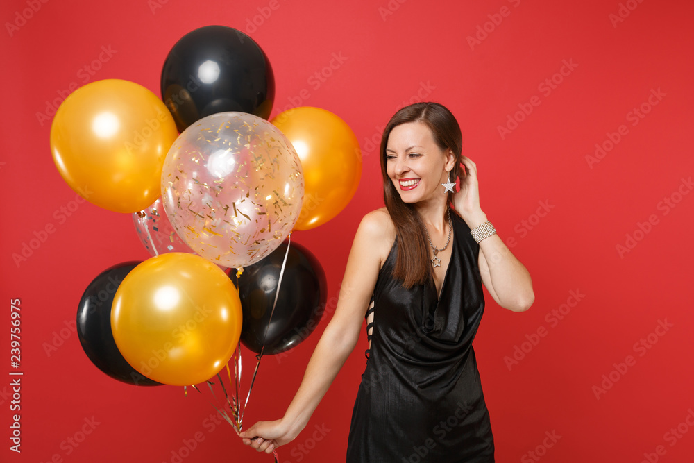 Fototapeta premium Pretty young woman in little black dress celebrating holding air balloons isolated on red background. St. Valentine's, International Women's Day, Happy New Year, birthday mockup holiday party concept.