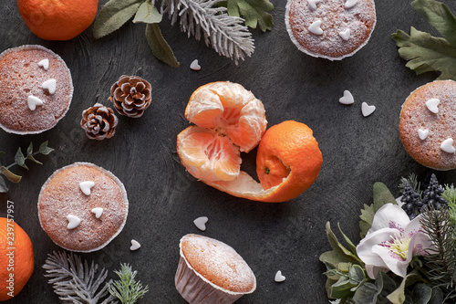 Top view of the table with satsumas, sugar-sprinkled muffins and Christmas star cookies on dark