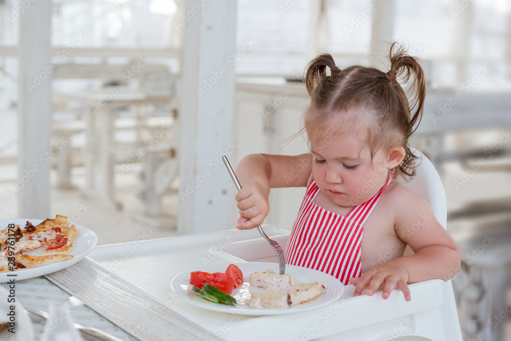 A little smiling toddler girl is sitting at a table in a summer cafe in the seaside resort. A little smiling toddler girl is sitting at a table in a summer cafe in the seaside resort.