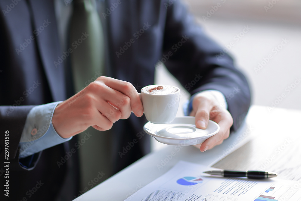 closeup of a young businessman with a cup of coffee in his hand checks some charts