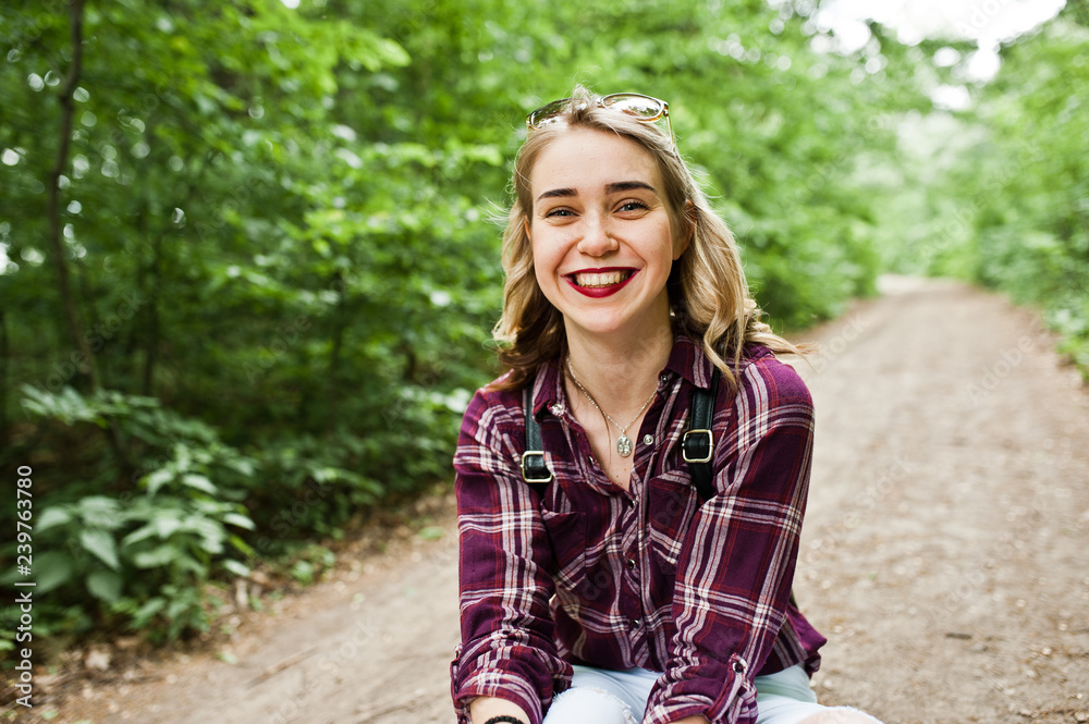 Portrait of a beautiful blond girl in tartan shirt sitting on the ground in the countryside. Portrait of a beautiful blond girl in tartan shirt sitting on the ground in the countryside.