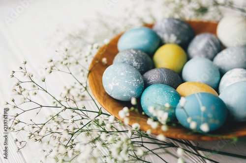 Canvas Print Stylish easter eggs with spring flowers on wooden plate on white wooden background