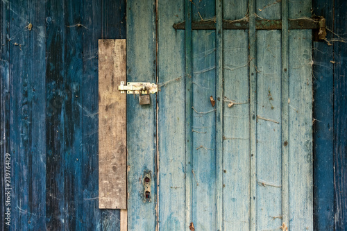 blaue tükise alte Holz Bretterwand enes Schuppens mit verschlossener und verriegelter Tür mit rustikaler Holzmaserung, Vorhängeschloss und vielen kleinen Spinnennetzen