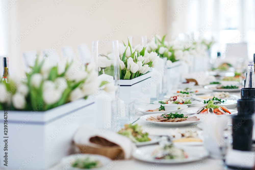 Dinner table serving. White tulips stand in flowerpots on white table served with delicious food