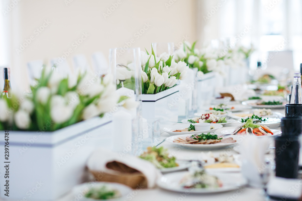 Dinner table serving. White tulips stand in flowerpots on white table served with delicious food Dinner table serving. White tulips stand in flowerpots on white table served with delicious food