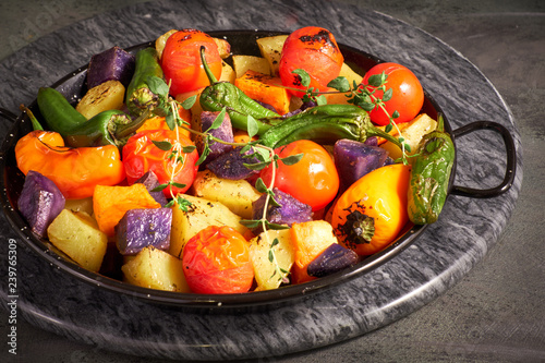 Rustic, oven baked vegetables in baking dish. Seasonal vegetarian vegan meal on dark stone board