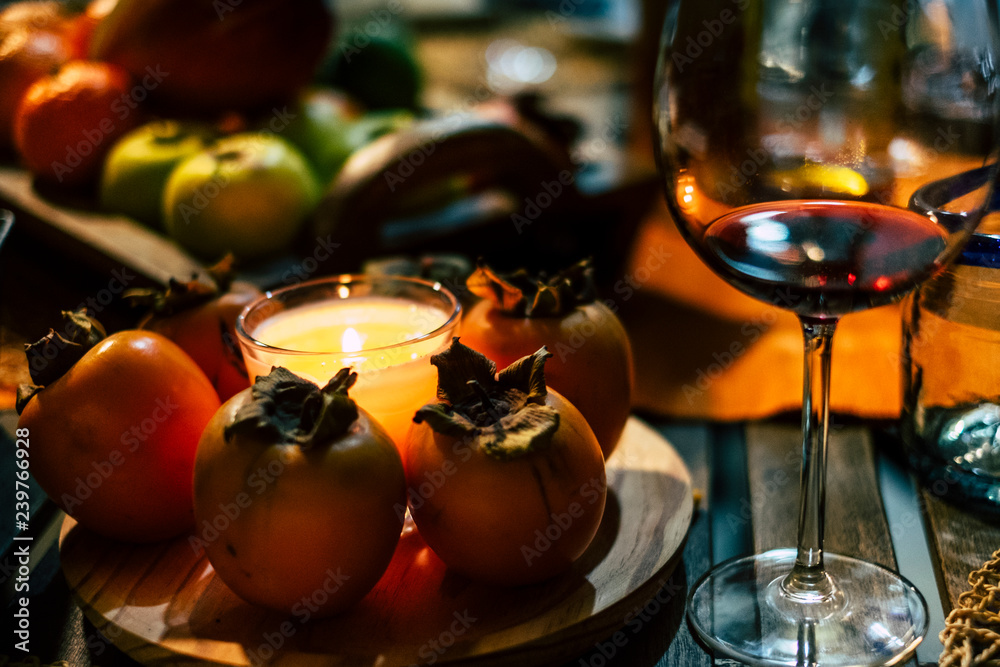 Winter style close up table with persimon fruits and red cup of wine - dark shadows and candle light for amazing evening atmosphere - christmas and new year eve concept -